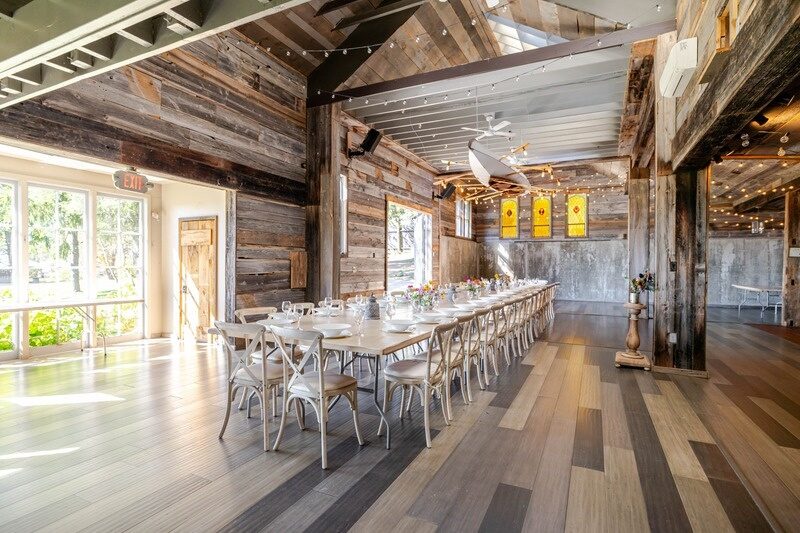 A long harvest table set in the barn at Twelve Ponds, cross-back chairs, string lights and vaulted ceiling.
