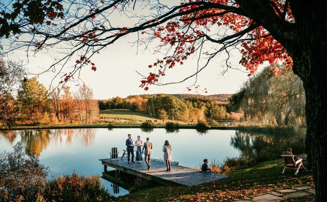 A small wedding ceremony on a wooden dock at Twelve Ponds, overlooking a still pond at sunset, with rolling hills in the background.