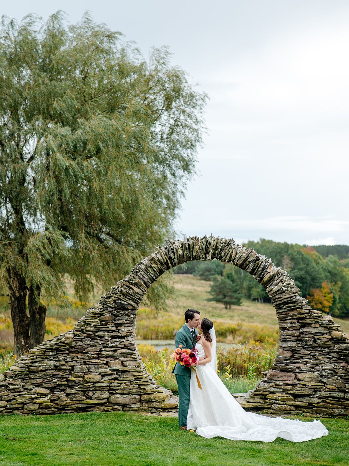 A couple at the stone moon gate in the meadow at Twelve Ponds.